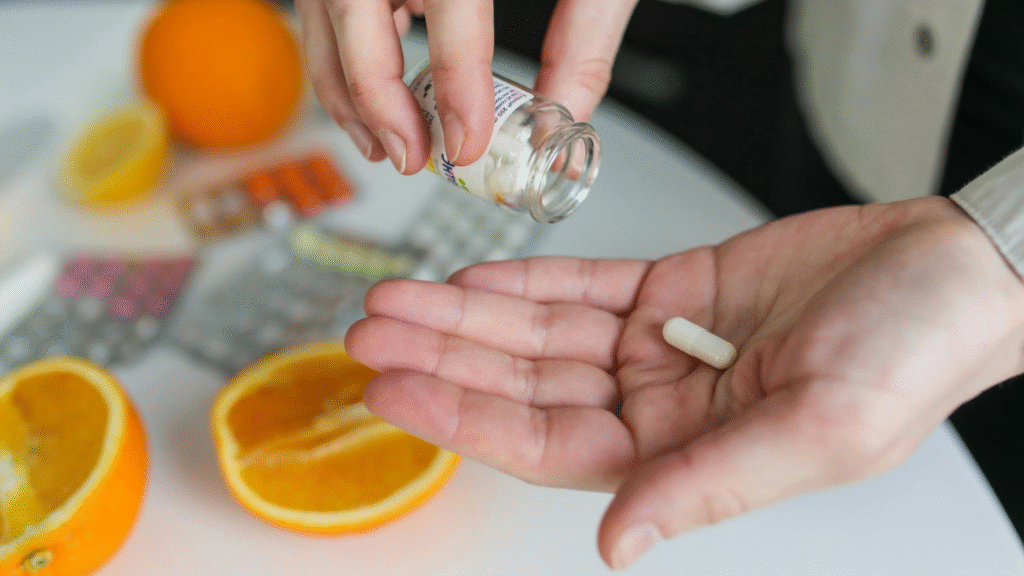 A person holding a white supplement capsule with sliced oranges and blister packs in the background — raising the question: Are supplements helping you maintain your health?-Search your fitness